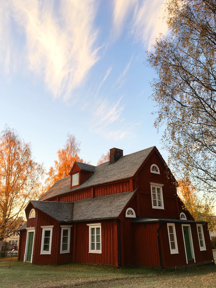 heros-img Picturesque red wooden house in autumn. Traditional Swedish architecture amidst colorful foliage.